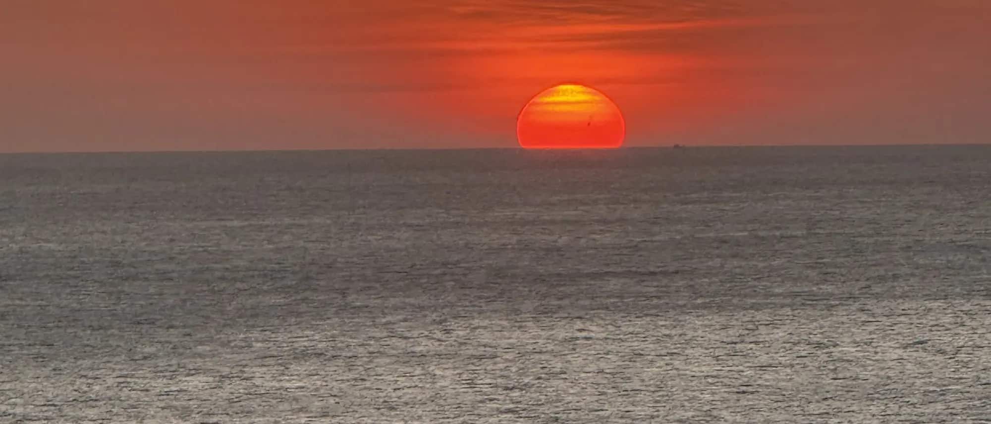 Le disque du soleil qui touche l'horizon au large de Phuket, la mer d'Andaman au premier plan