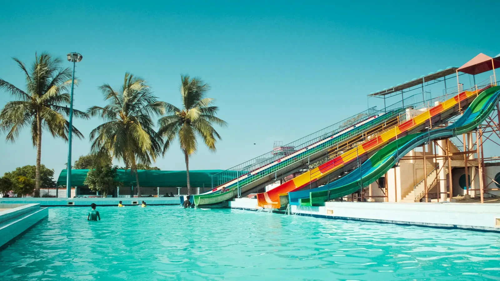 Colourful slides plunging into the big turquoise pool of a water park, under coconut palms