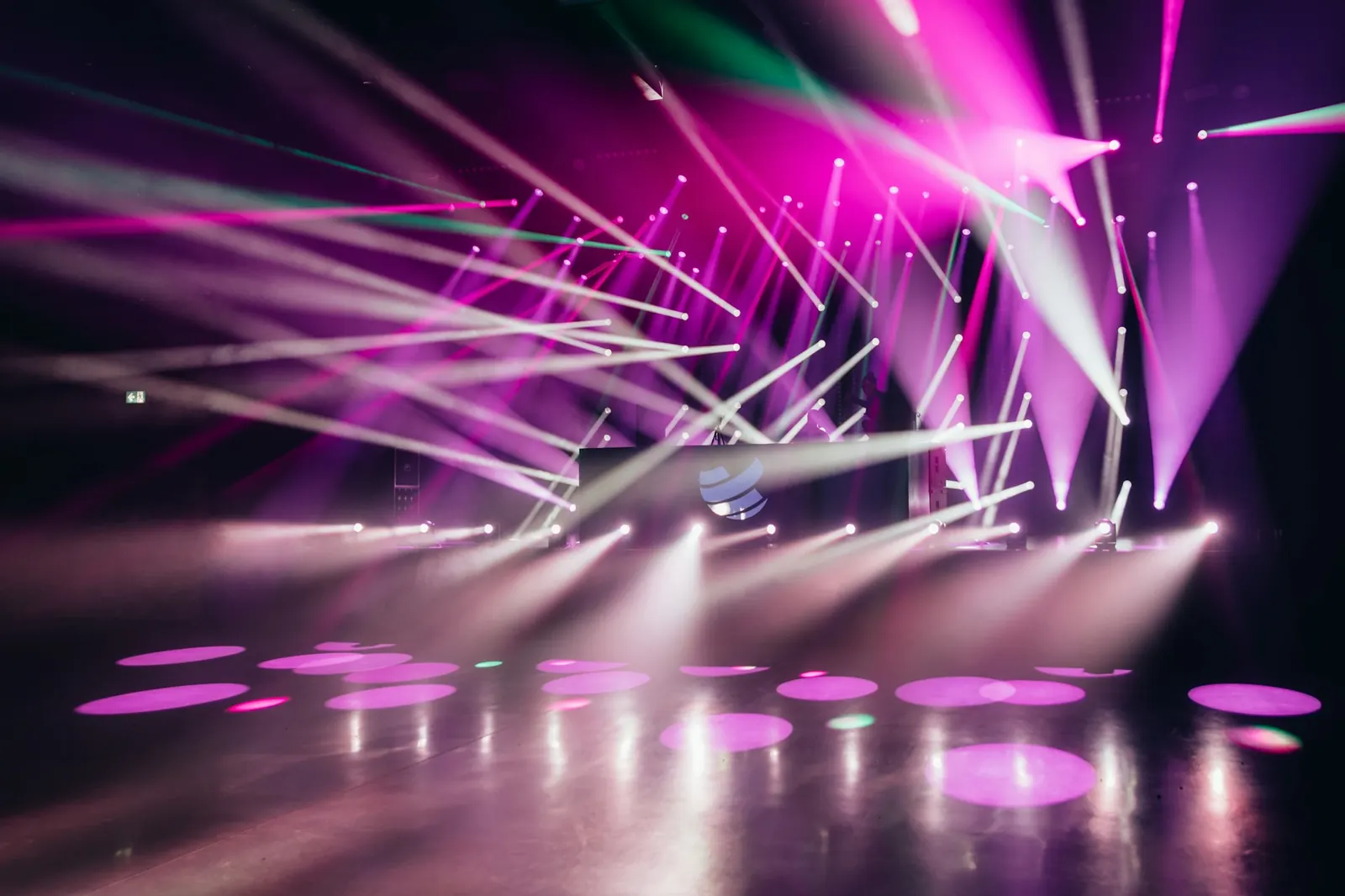 Scène de spectacle balayée de faisceaux de projecteurs roses et blancs, cercles de lumière sur le plateau