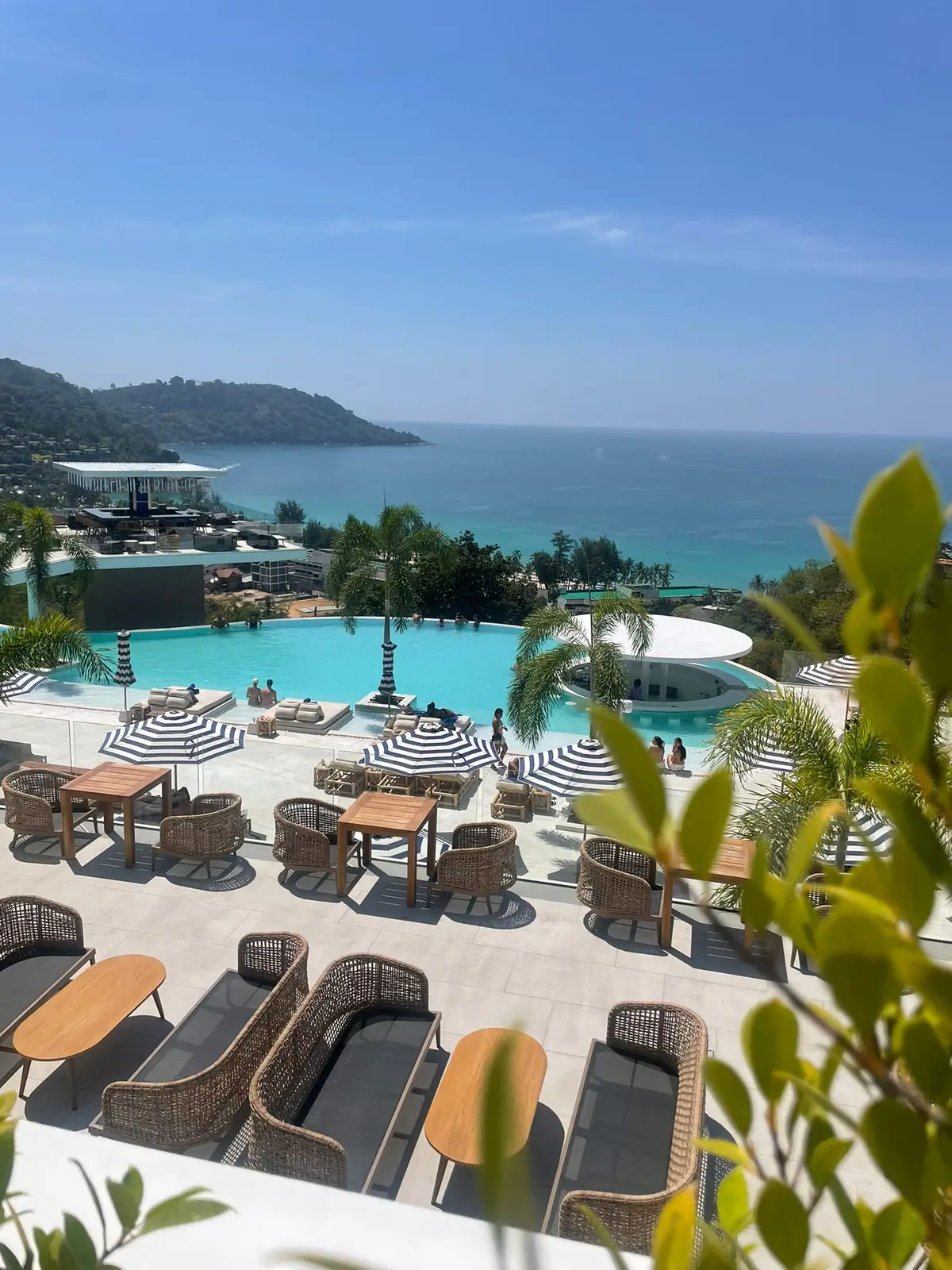 Grande piscine d'un beach club de Phuket bordée de transats et de parasols rayés, face à la mer