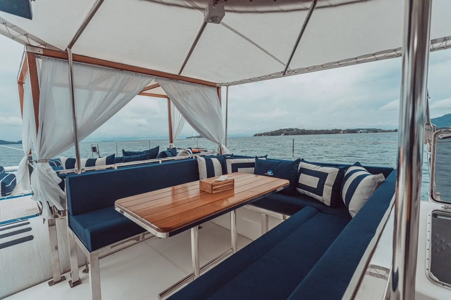 Carré intérieur d'un catamaran à Phuket : banquettes en U, coussins bleus et table en bois clair