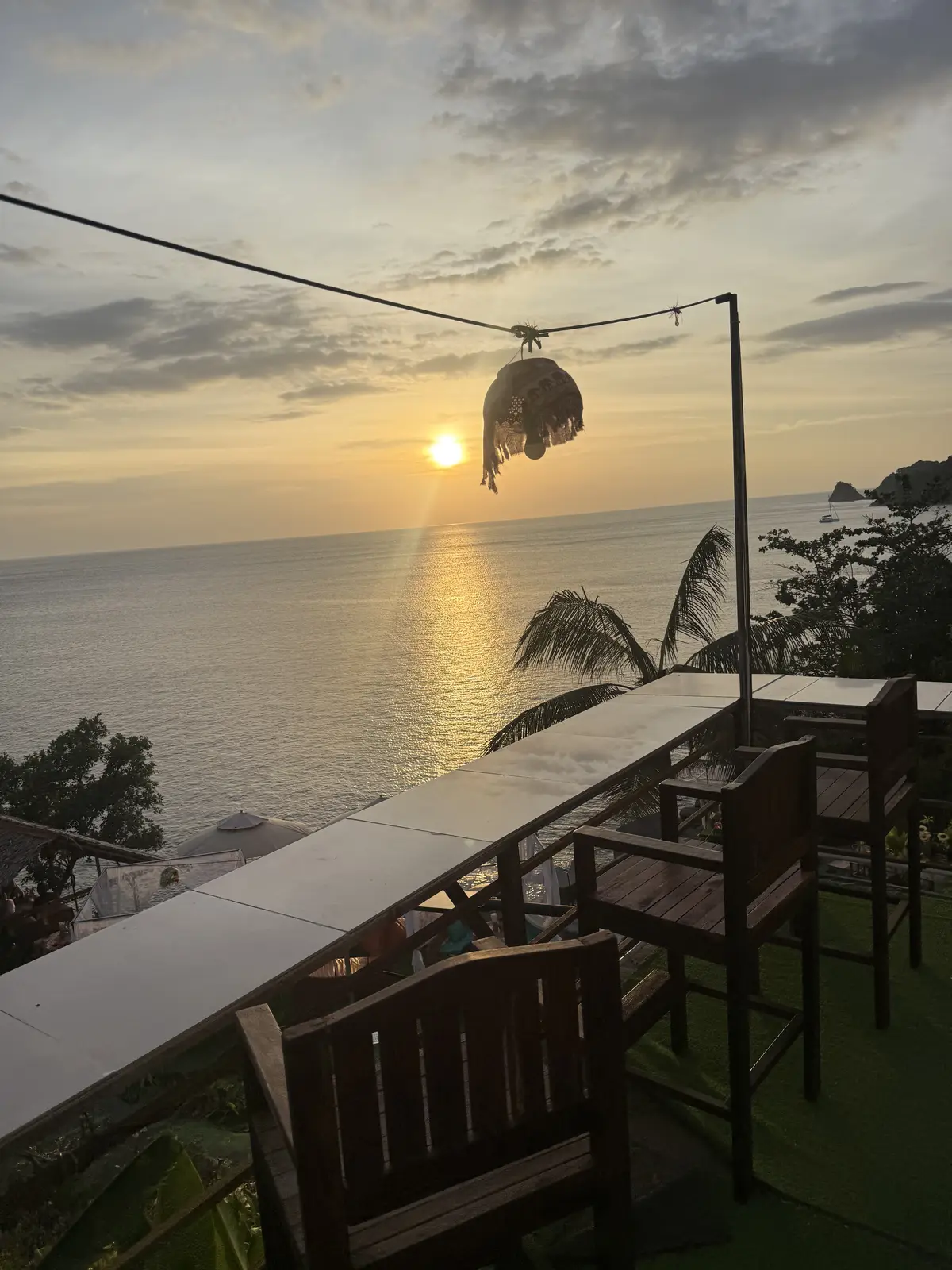 Table et chaises en bois sur une terrasse de Phuket au coucher du soleil, la mer d'Andaman en contrebas