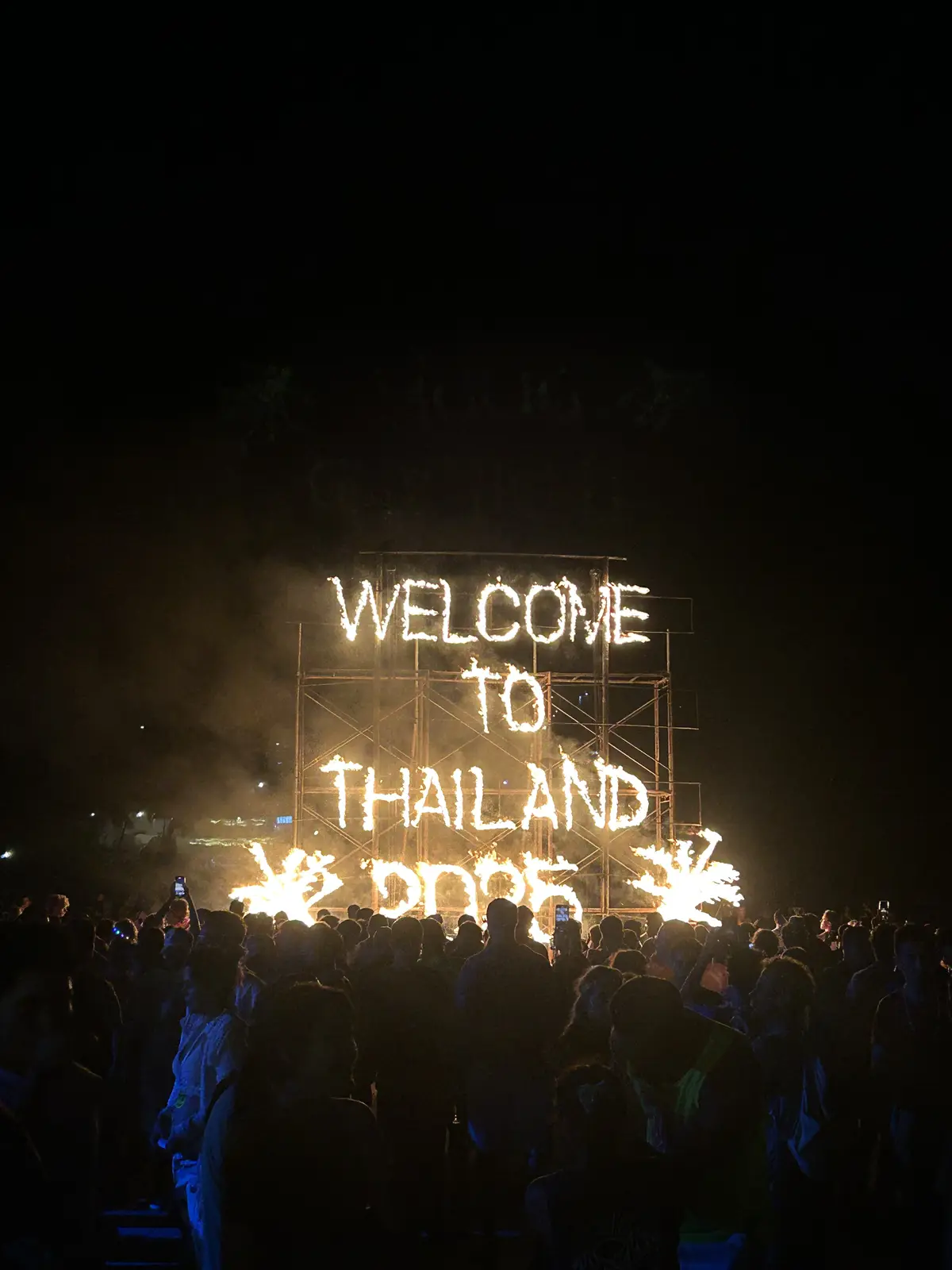 Enseigne lumineuse « Welcome to Thailand » au-dessus d'une foule, lors d'une soirée en plein air
