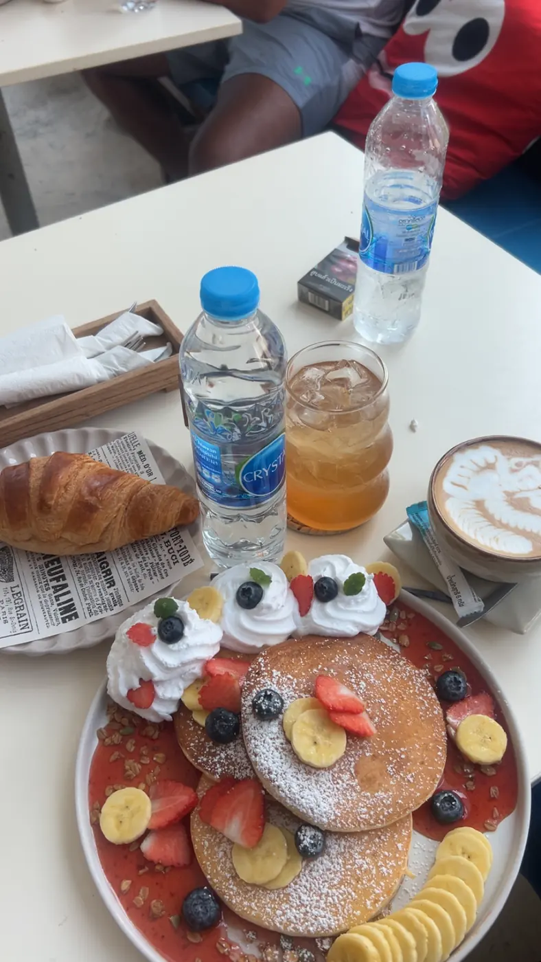 Pancakes with fresh fruit, a croissant, a cappuccino and juice on a café table in Phuket