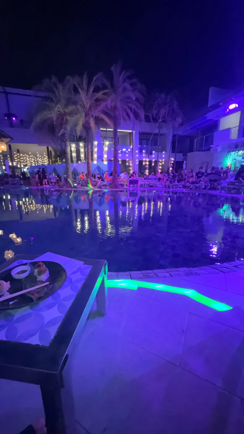 Piscine éclairée en bleu et violet d'un club en plein air à Patong, palmiers illuminés, de nuit