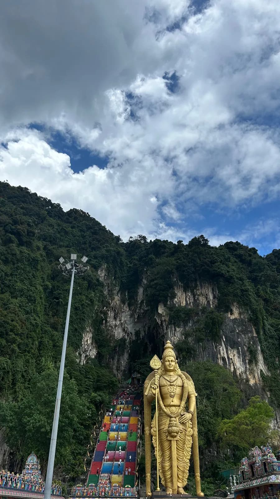 La statue dorée de Murugan et l'escalier multicolore des Batu Caves, sous la falaise