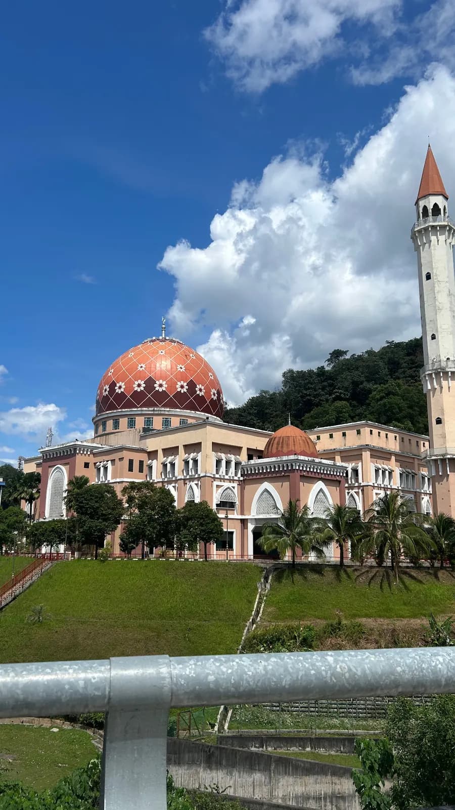 Mosquée au dôme orange fleuri et minaret blanc, sur une colline verte, à Putrajaya