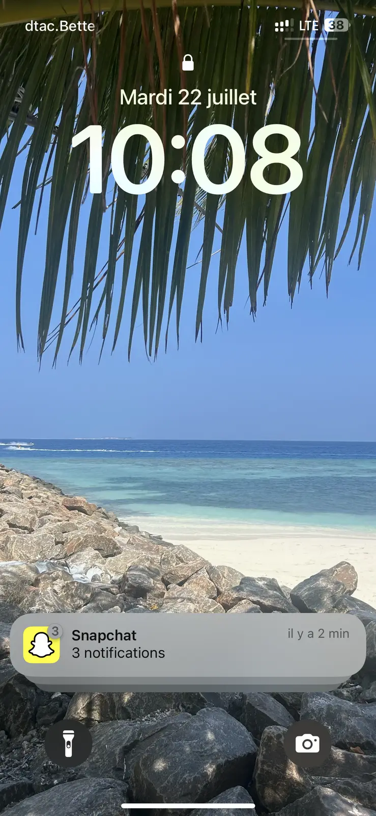 Plage de sable blanc et eau turquoise vue à travers des palmes, sur une île proche de Phuket