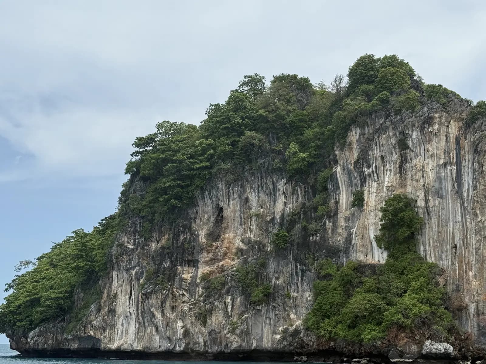 Piton rocheux couvert de végétation sortant de la mer, sous un ciel dégagé, au large de Phuket