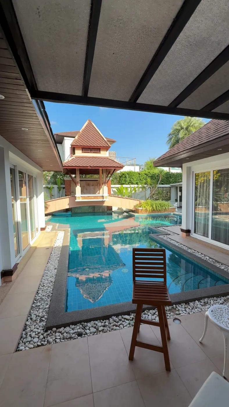 A private pool between two wings of a Thai-roofed villa, a wooden chair at the water's edge
