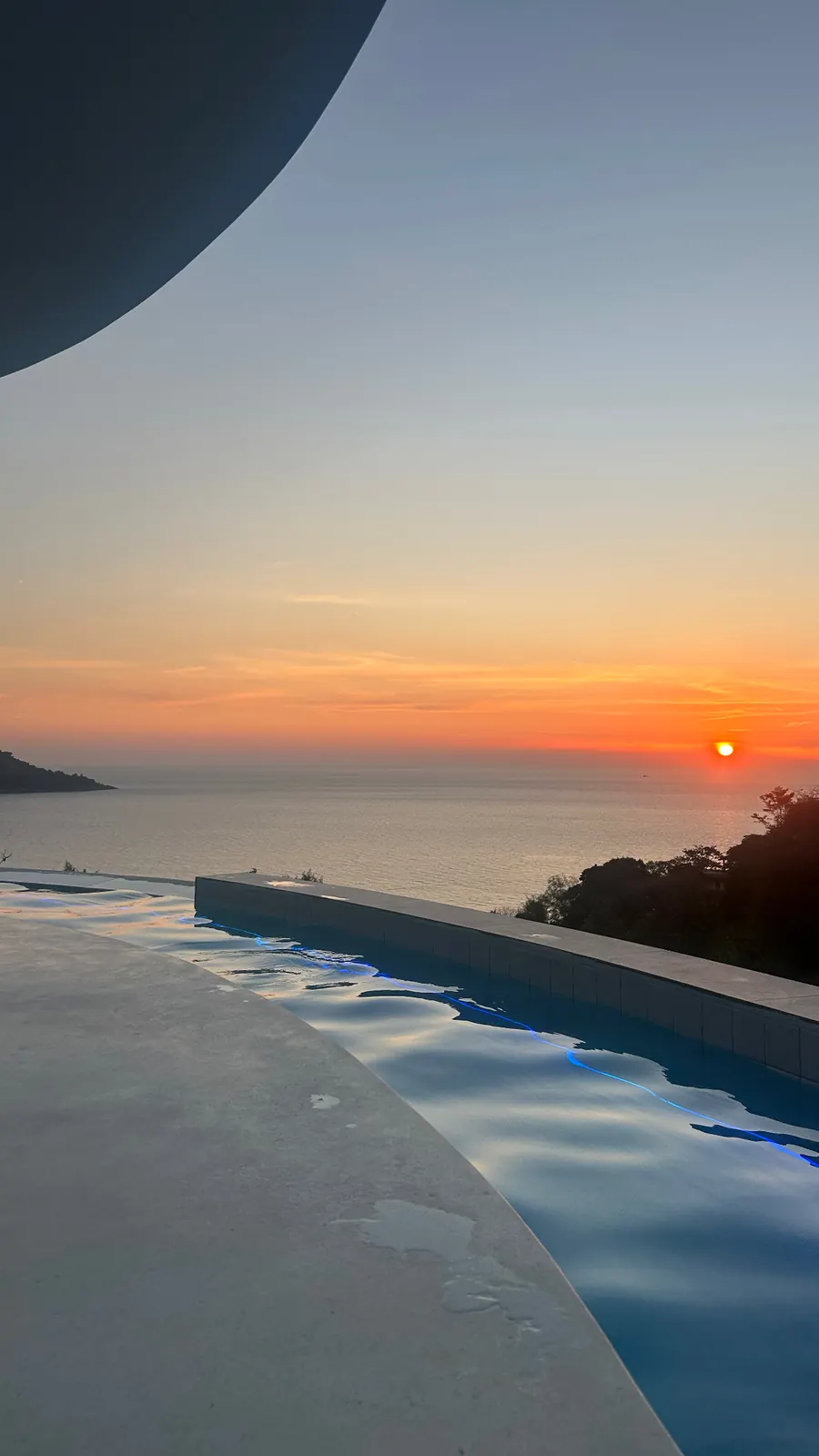 Infinity pool of a hillside villa facing the sunset over the sea